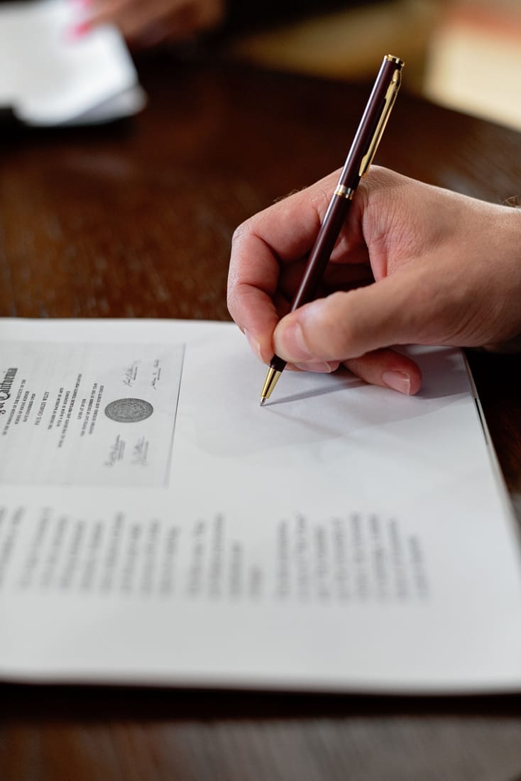 A person signing an official document with a pen during a mobile notary appointment