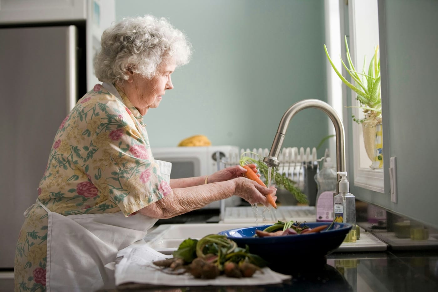 A senior woman washing fresh vegetables at her kitchen sink at home